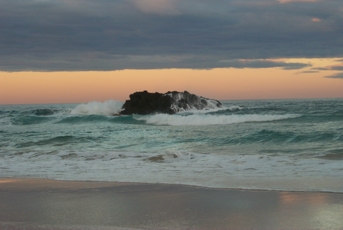 The sun going down over rocks in the surf at Wooyung Beach.